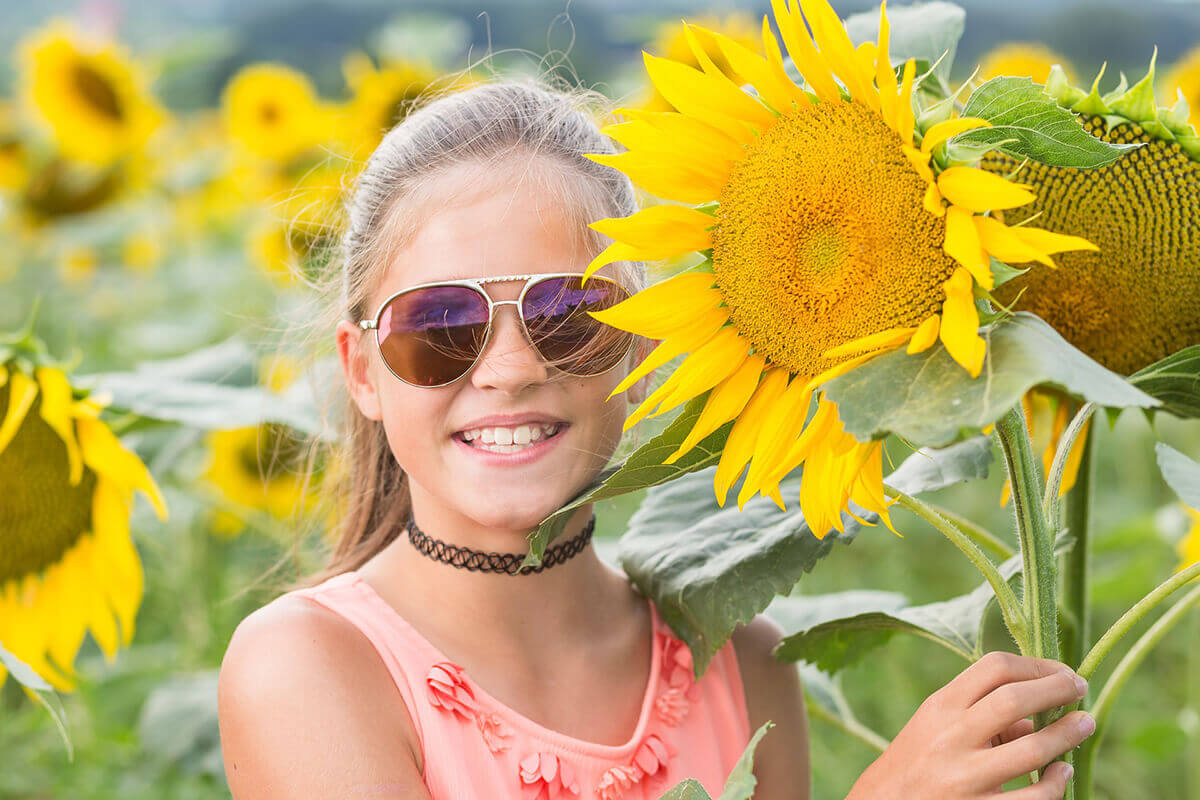 Lachendes Kind mit Sonnenbrille und Sonnenblume