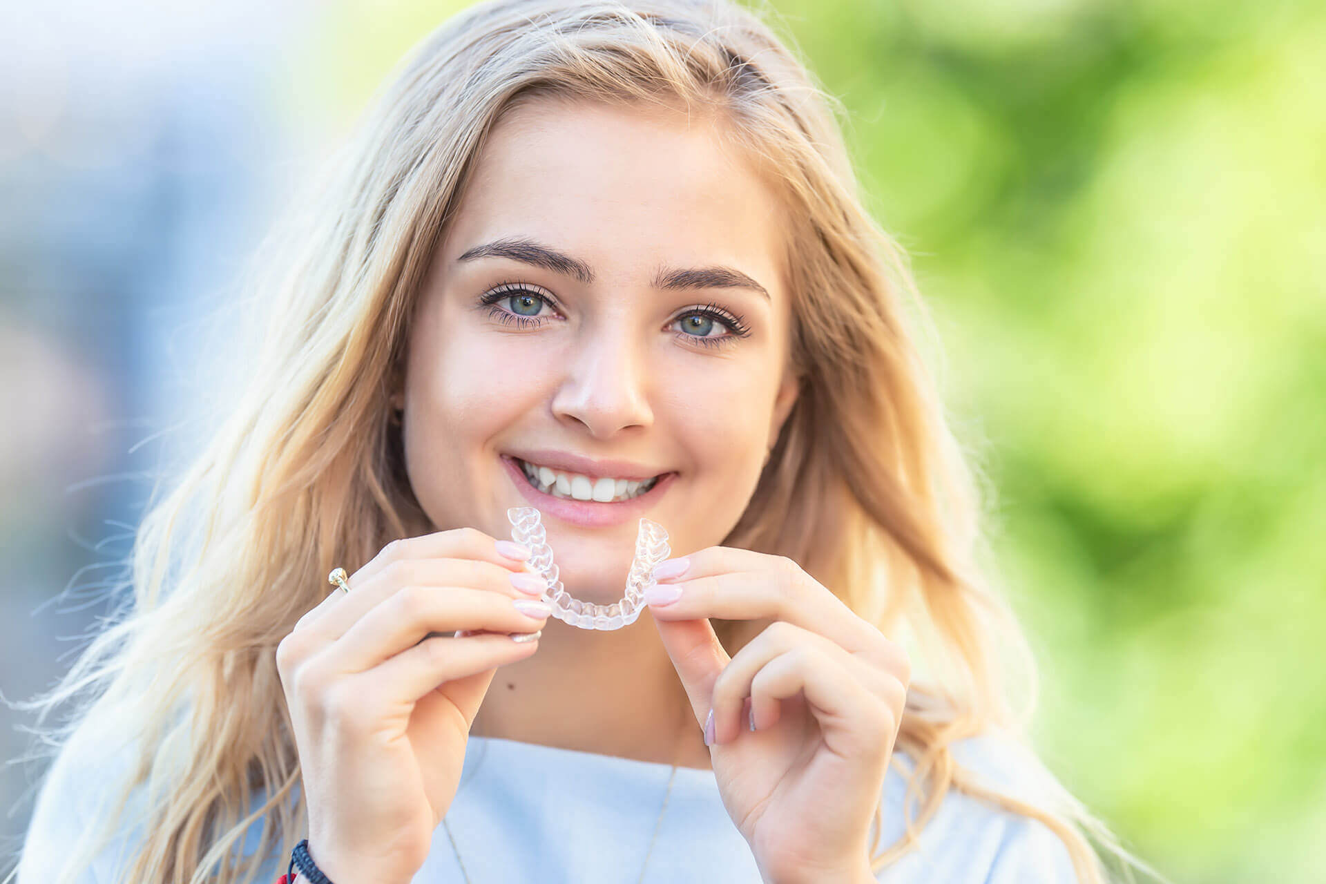 Maedchen laechelt mit Aligner in der Hand